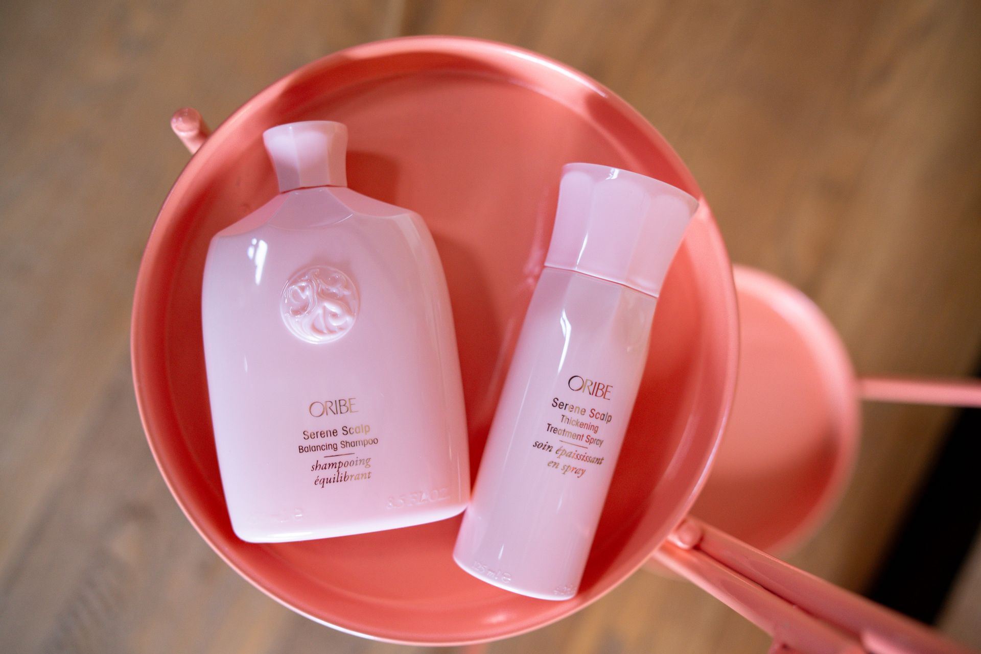 Pink Oribe Serene Balancing Shampoo and Thickening Treatment Spray bottles sitting in pink pot.